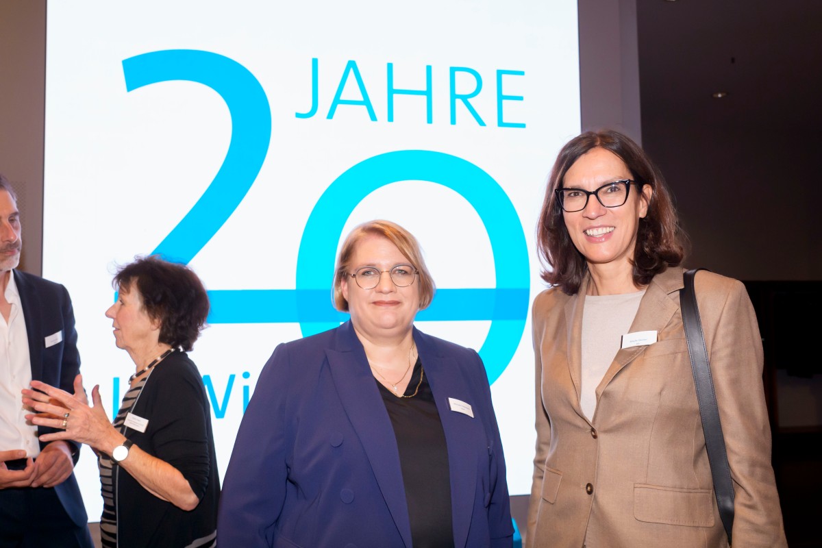 Die stellvertretende Institutsleiterin Michaela Eikermann steht neben Sibylle Steiner von der Kassenärztlichen Bundesvereinigung vor dem Jubiläumslogo des IQWiG.