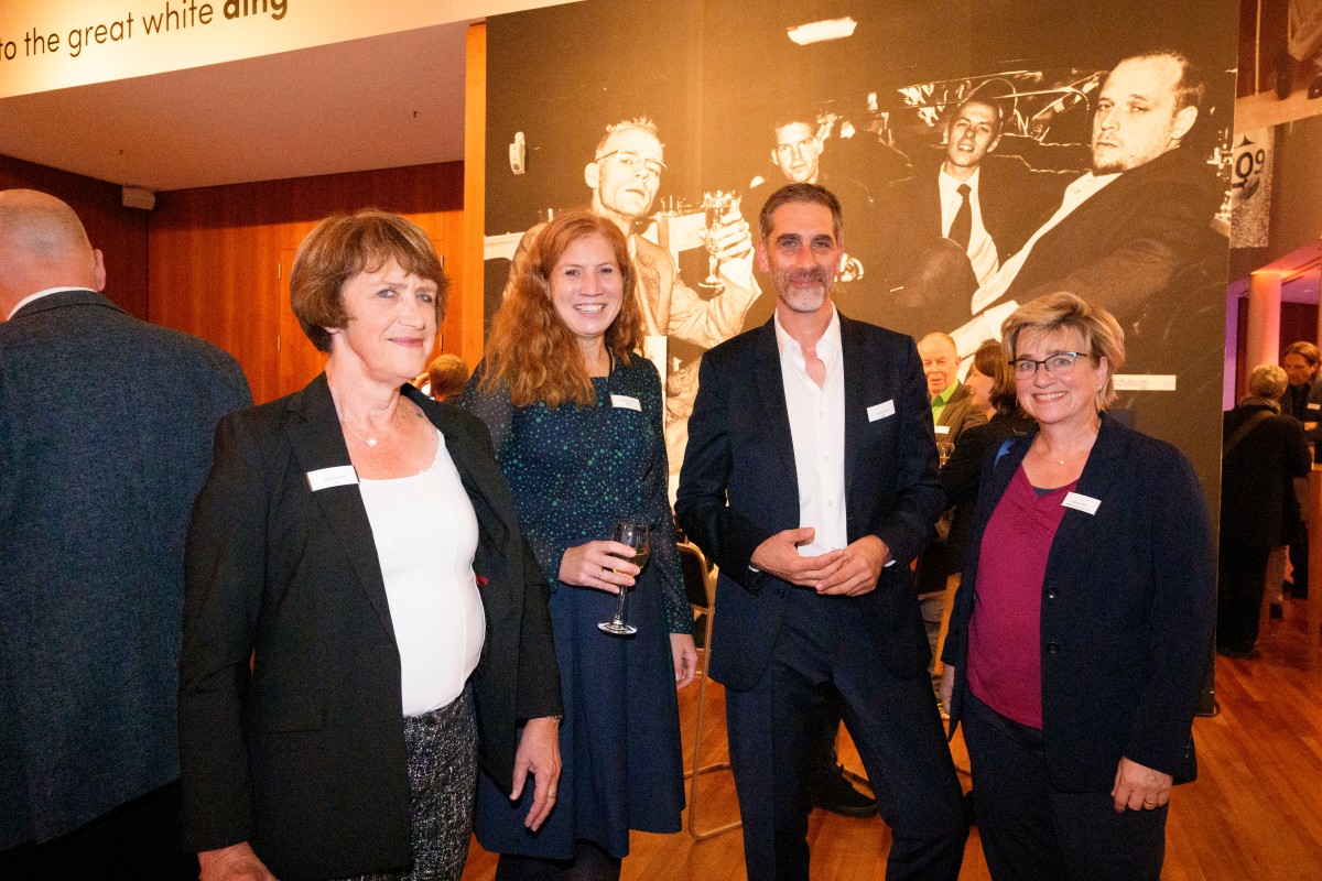 Doris Pfeiffer (GKV-Spitzenverband), Johanna Sell (Bundesministerium für Gesundheit), Thomas Kaiser (IQWiG) und Kerstin Haid (Medizinischer Dienst Bund) vor einem großen Foto der Ausstellung.