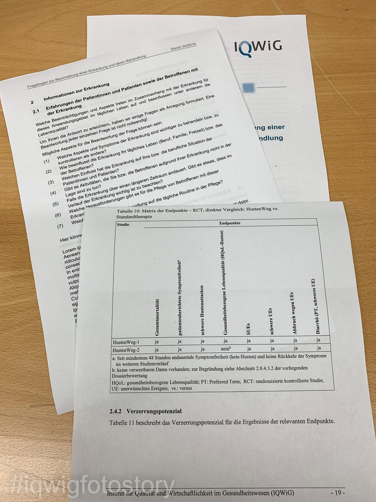 Zwei Blätter aus einem ausgefüllten Patientenfragebogen und eine Endpunkt-Tabelle aus dem Entwurf der Dossierbewertung auf einem Schreibtisch.